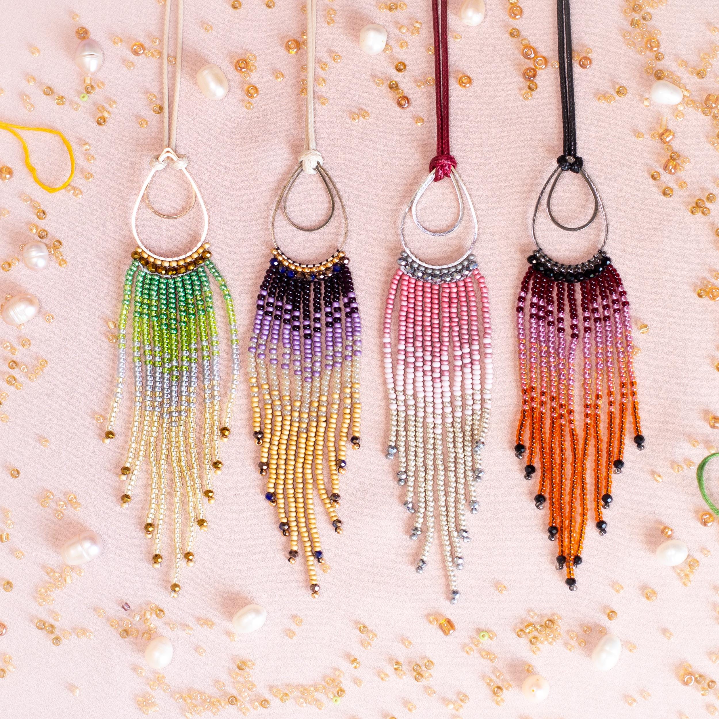 a collection of colorful beaded necklaces with long tassels hanging from them, arranged on a pink background with scattered pearls.